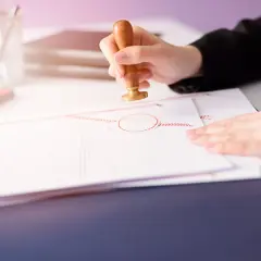Dłoń z pieczęcią nad dokumentem. Sprawdzanie, jakie dokumenty do sprzedaży mieszkania są potrzebne, to ważny etap transakcji.