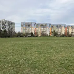 Dwa długie bloki mieszkalne, każdy dom z wielkiej płyty, stoją na tle zielonego trawnika i nieba.