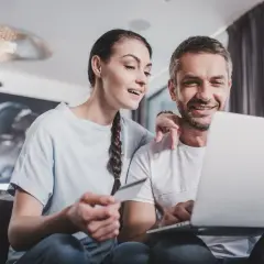 Para sprawdzająca dewelopera przed kupnem mieszkania, analizująca dane na laptopie i trzymająca kartę.