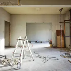 Trwa wyburzanie ścian działowych. Widać drabiny, gruz i narzędzia budowlane.