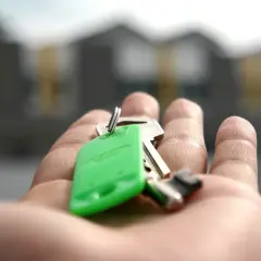 Dłoń trzymająca klucze do domu na tle budynków.