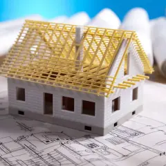 Model domu na planach budowlanych. Czy adaptacja projektu jest konieczna? W tle zwoje dokumentacji.