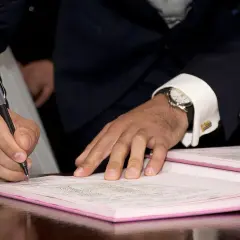 Mężczyzna w garniturze podpisuje dokumenty, co może oznaczać wypowiedzenie umowy najmu mieszkania za porozumieniem stron.