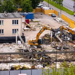 Koparki pracują na placu budowy, rozbierając budynek. Zastanawiasz się, ile kosztuje rozbiórka domu?