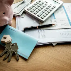 Klucze do mieszkania, skarbonka i rachunki na stole sugerują, co wchodzi w skład czynszu za mieszkanie własnościowe.