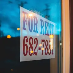 Szyld "FOR RENT" na szybie, z numerem telefonu. Ktoś szuka okazji do wynajmu lub najmu.