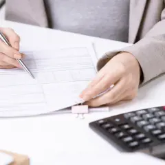 Osoba z długopisem analizuje dokumenty, obok leży kalkulator. To może być związane z tym, co to jest zaliczka eksploatacyjna.