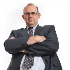 Mężczyzna w garniturze i okularach ze skrzyżowanymi rękami.