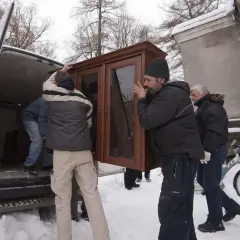 Mężczyźni wynoszą mebel z vana w śnieżny dzień. Może to być przeprowadzka lub zabezpieczenie mienia przed eksmisją.