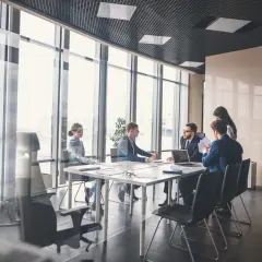 Dyskusja o tym, ile zarabia członek zarządu spółdzielni mieszkaniowej, podczas spotkania biznesowego w nowoczesnym biurze z widokiem na miasto.