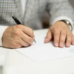 Mężczyzna w eleganckim garniturze pisze piórem na białej kartce, składając wniosek o wydanie listu mazalnego.