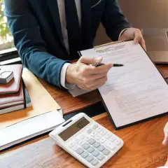 Doradca omawia z klientem umowę, porównując kredyt gotówkowy czy hipoteczny. Na biurku kalkulator i model domu.