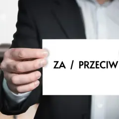 Mężczyzna w garniturze trzyma kartkę z napisem "ZA / PRZECIW". Dylemat, kiedy uchwała wspólnoty mieszkaniowej jest nieważna.