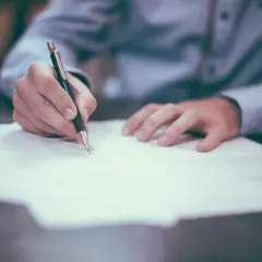 Dłoń pisze długopisem na papierze, przygotowując podanie do spółdzielni mieszkaniowej.