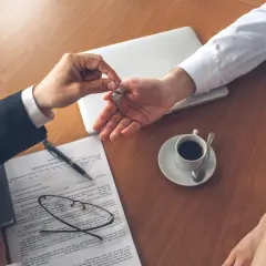 Przekazanie kluczy do mieszkania. Podpisanie umowy, kawa i laptop sugerują transakcję, być może związaną z kaucją za wynajem mieszkania.