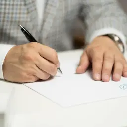 Mężczyzna w eleganckim garniturze pisze piórem na białej kartce, składając wniosek o wydanie listu mazalnego.