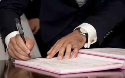 Mężczyzna w garniturze podpisuje dokumenty, co może oznaczać wypowiedzenie umowy najmu mieszkania za porozumieniem stron.