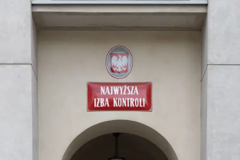 Tablica z napisem "Najwyższa Izba Kontroli" i godłem Polski na jasnym budynku.