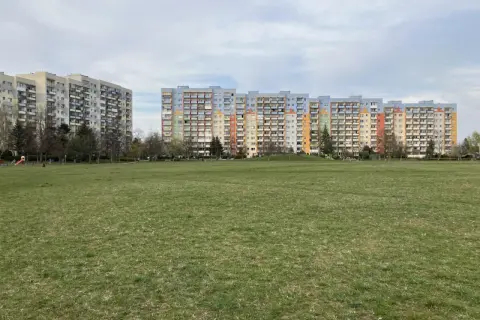 Dwa długie bloki mieszkalne, każdy dom z wielkiej płyty, stoją na tle zielonego trawnika i nieba.