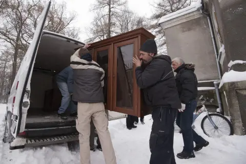 Mężczyźni wynoszą mebel z vana w śnieżny dzień. Może to być przeprowadzka lub zabezpieczenie mienia przed eksmisją.