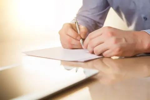 Mężczyzna pisze piórem na kartce papieru. To może być list mazalny, który jest ważnym dokumentem.