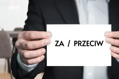 Mężczyzna w garniturze trzyma kartkę z napisem "ZA / PRZECIW". Dylemat, kiedy uchwała wspólnoty mieszkaniowej jest nieważna.