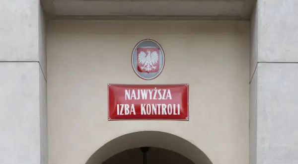 Tablica z napisem "Najwyższa Izba Kontroli" i godłem Polski na jasnym budynku.