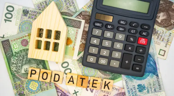 Drewniany domek, banknoty i kalkulator sugerują, ile wynosi podatek od nieruchomości.