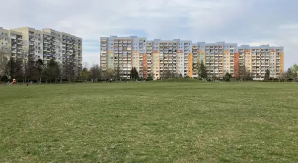 Dwa długie bloki mieszkalne, każdy dom z wielkiej płyty, stoją na tle zielonego trawnika i nieba.