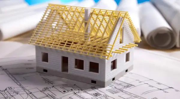 Model domu na planach budowlanych. Czy adaptacja projektu jest konieczna? W tle zwoje dokumentacji.