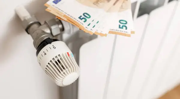 Termostat grzejnikowy i banknoty 50 euro. Obrazek ilustruje, jak spółdzielnia rozlicza ogrzewanie, pokazując koszty związane z ciepłem.