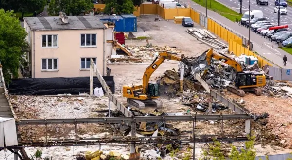 Koparki pracują na placu budowy, rozbierając budynek. Zastanawiasz się, ile kosztuje rozbiórka domu?