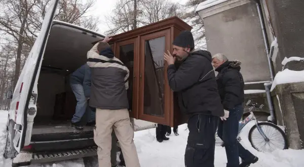 Mężczyźni wynoszą mebel z vana w śnieżny dzień. Może to być przeprowadzka lub zabezpieczenie mienia przed eksmisją.