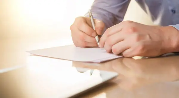Mężczyzna pisze piórem na kartce papieru. To może być list mazalny, który jest ważnym dokumentem.