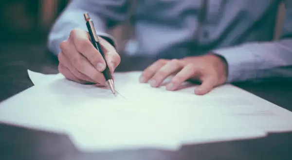 Dłoń pisze długopisem na papierze, przygotowując podanie do spółdzielni mieszkaniowej.