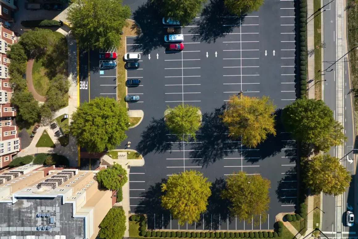 Widok z lotu ptaka na parking przy blokach mieszkalnych. Zastanawiasz się, ile miejsc parkingowych na mieszkanie jest dostępne?