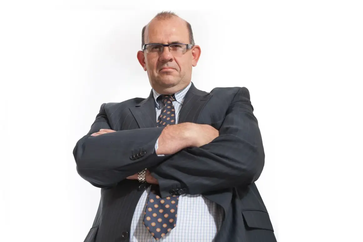 Mężczyzna w garniturze i okularach ze skrzyżowanymi rękami.