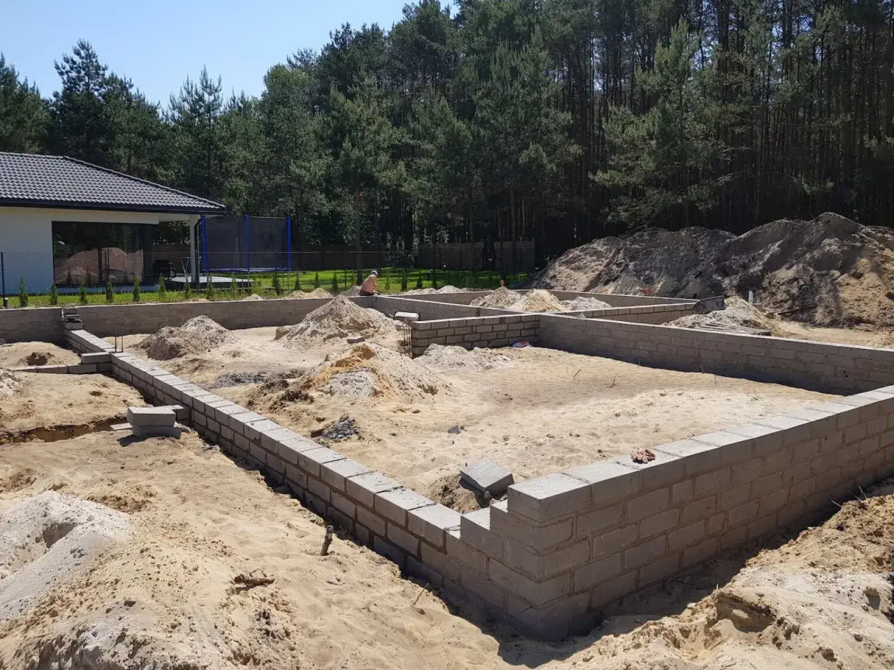 Fundamenty domu w budowie. Piasek, bloczki betonowe i widok na las. Marzenie o budowie domu samemu staje się rzeczywistością.