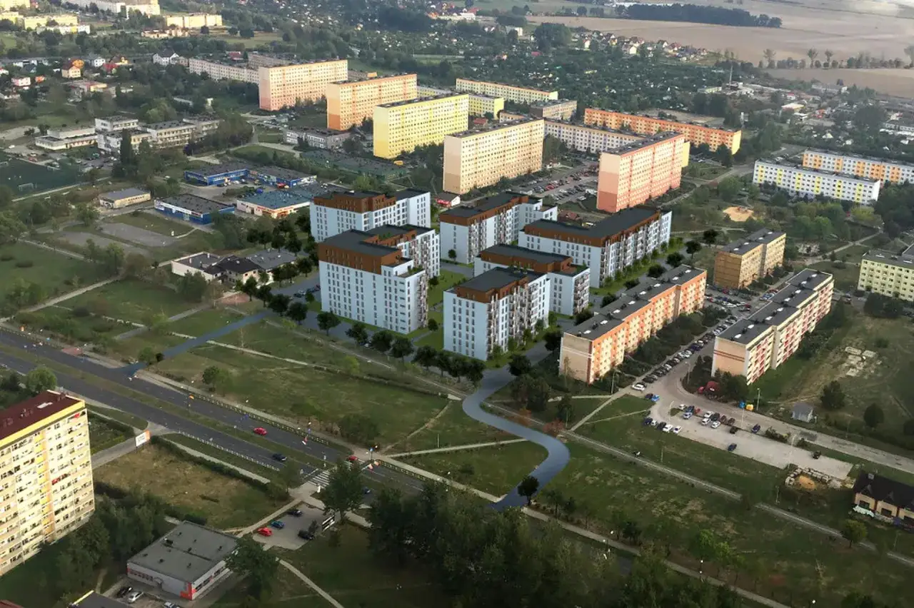 Osiedle z wielopiętrowymi blokami mieszkalnymi, ulicami i terenami zielonymi. Wizualizacja pokazuje, tbs co to znaczy - nowoczesne budownictwo.