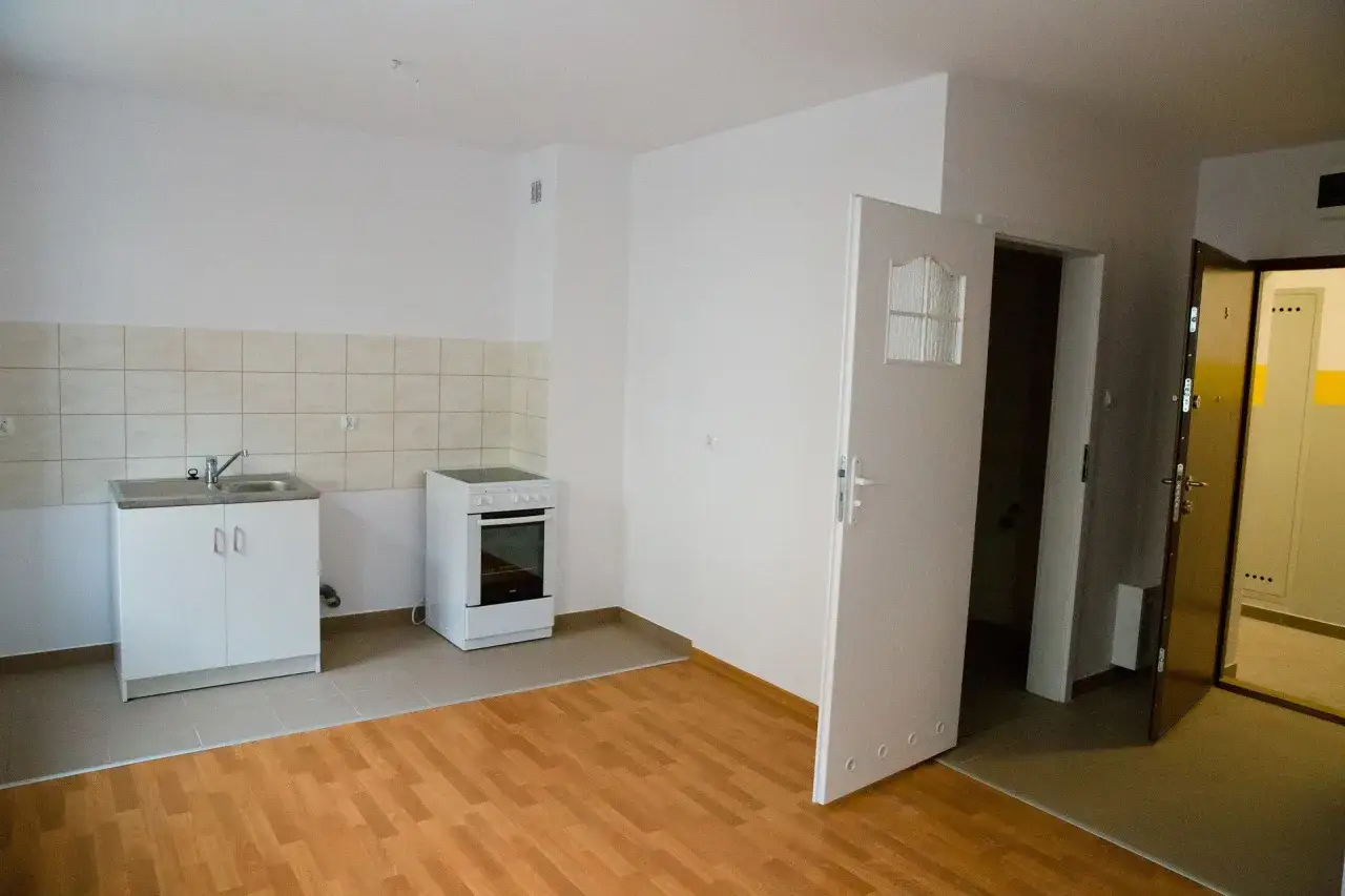 Proste, funkcjonalne mieszkania socjalne: kuchnia z kuchenką i zlewem, drzwi otwarte na korytarz.