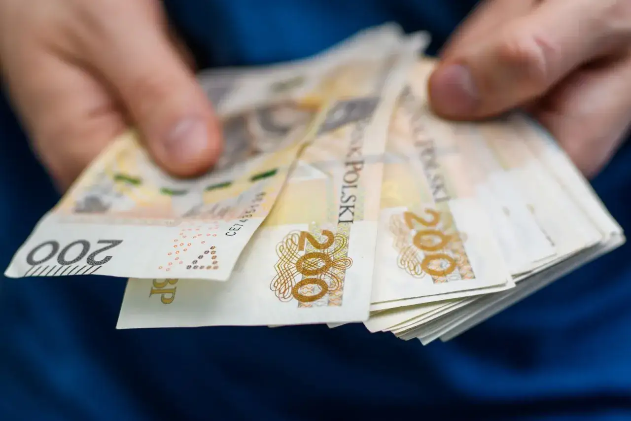 Dłonie trzymają stos banknotów 200 zł. Zastanawiasz się, ile wynosi czynsz za mieszkanie w bloku?