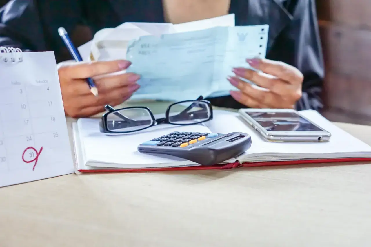 Kobieta analizuje dokumenty, obok leżą okulary, kalkulator i telefon. Czy od spadku po rodzicach płaci się podatek?