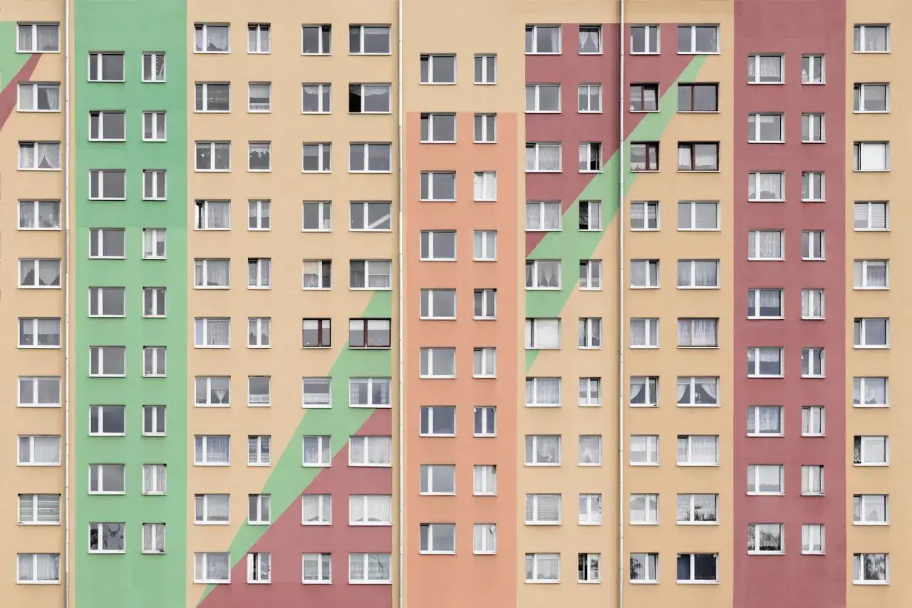 Wielopiętrowy blok mieszkalny z kolorowymi pasami. Okna w mieszkaniach spółdzielczych własnościowych tworzą rytmiczny wzór.
