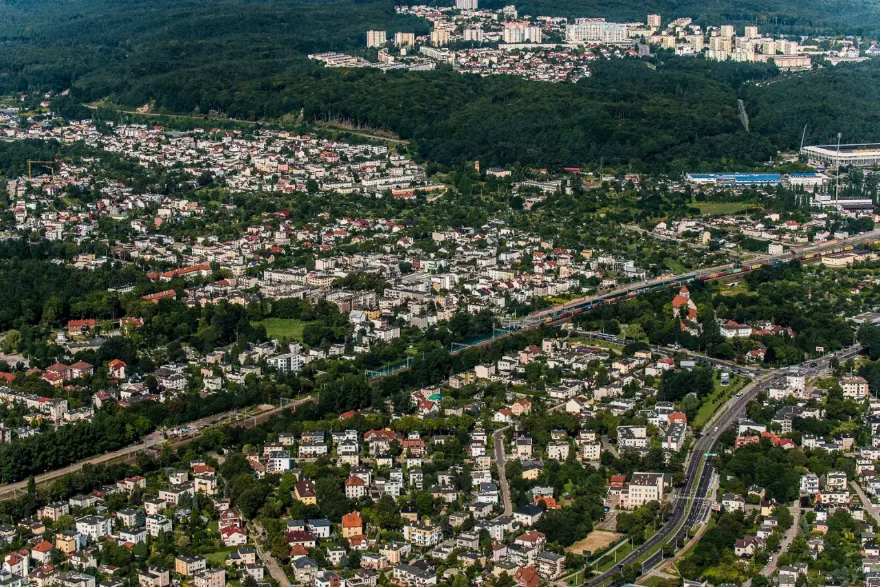 Widok z lotu ptaka na osiedla mieszkaniowe w Grudziądzu. Widać liczne domy, drzewa i drogę. TBS Grudziądz oferuje wolne mieszkania w tej okolicy.
