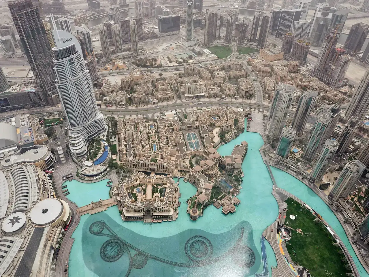 Widok z góry na Dubaj, z widocznym kompleksem budynków i wodnym placem. Z tej perspektywy trudno ocenić, jak wysoki jest Burj Khalifa, ale widać jego ogromną skalę.