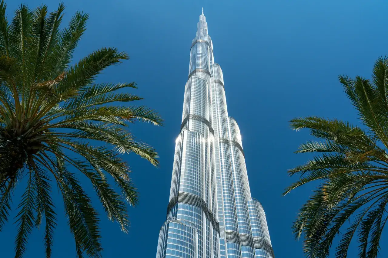 Burj Khalifa, najwyższy budynek świata, ma 828 metrów. Widok z dołu, z palmami po bokach, na błękitne niebo.