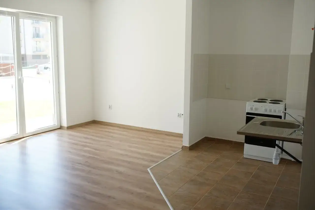 Proste, funkcjonalne mieszkania socjalne: kuchnia z kuchenką i zlewem, jasny pokój z dużym oknem.