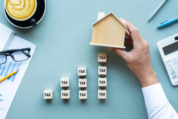 Domyślnie czy podatek od nieruchomości płaci się co roku? Drewniany domek na kostkach z napisem "TAX" symbolizuje roczne obciążenia.