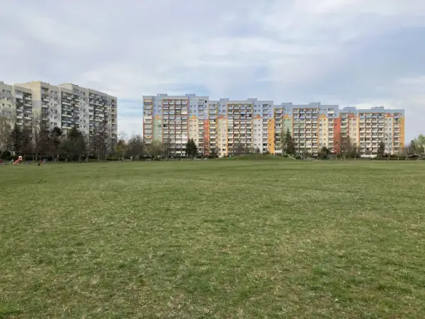 Dwa długie bloki mieszkalne, każdy dom z wielkiej płyty, stoją na tle zielonego trawnika i nieba.