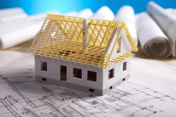 Model domu na planach budowlanych. Czy adaptacja projektu jest konieczna? W tle zwoje dokumentacji.